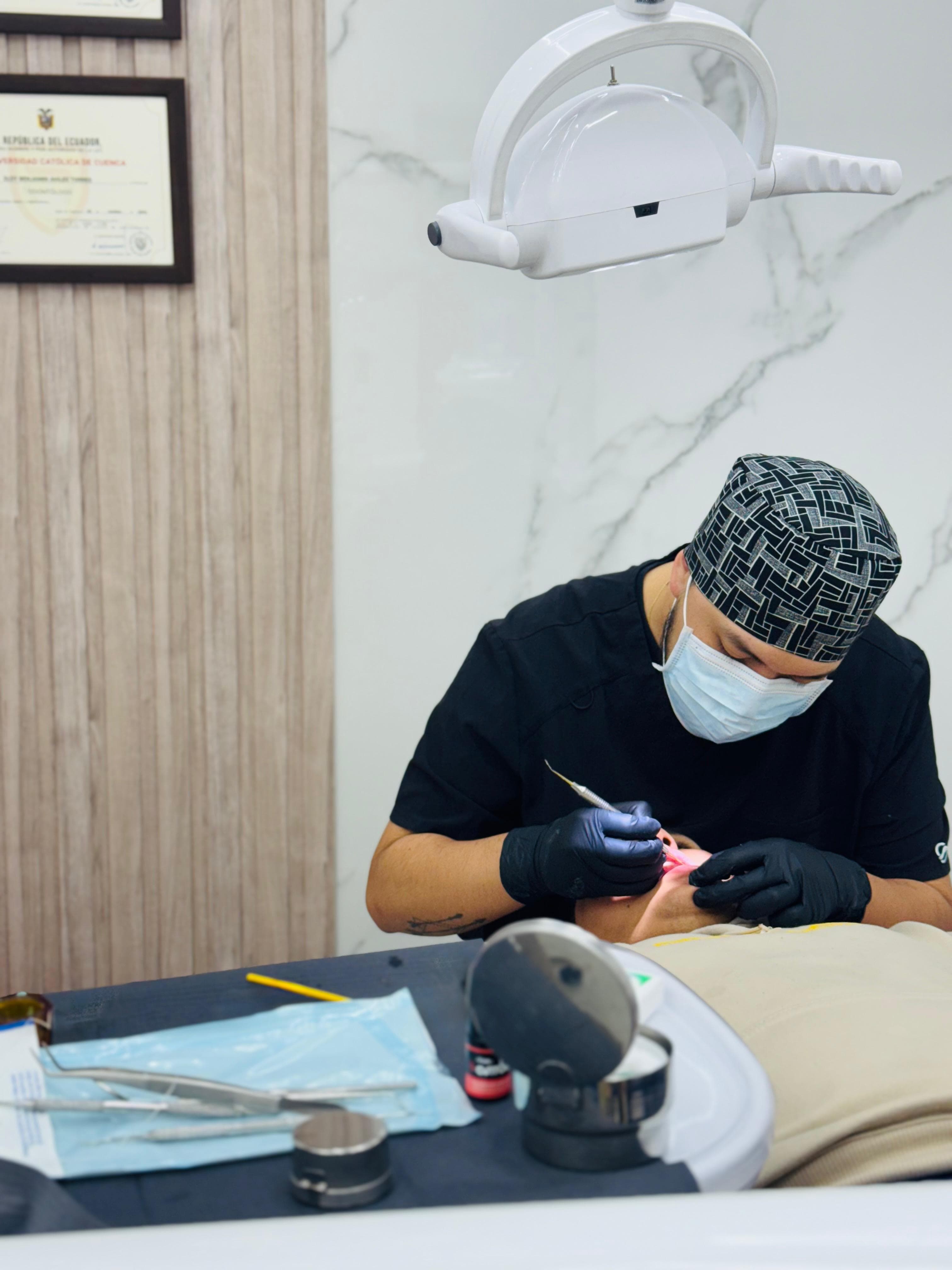 Dentist in black scrubs, mask, and patterned cap performs a procedure on a patient.