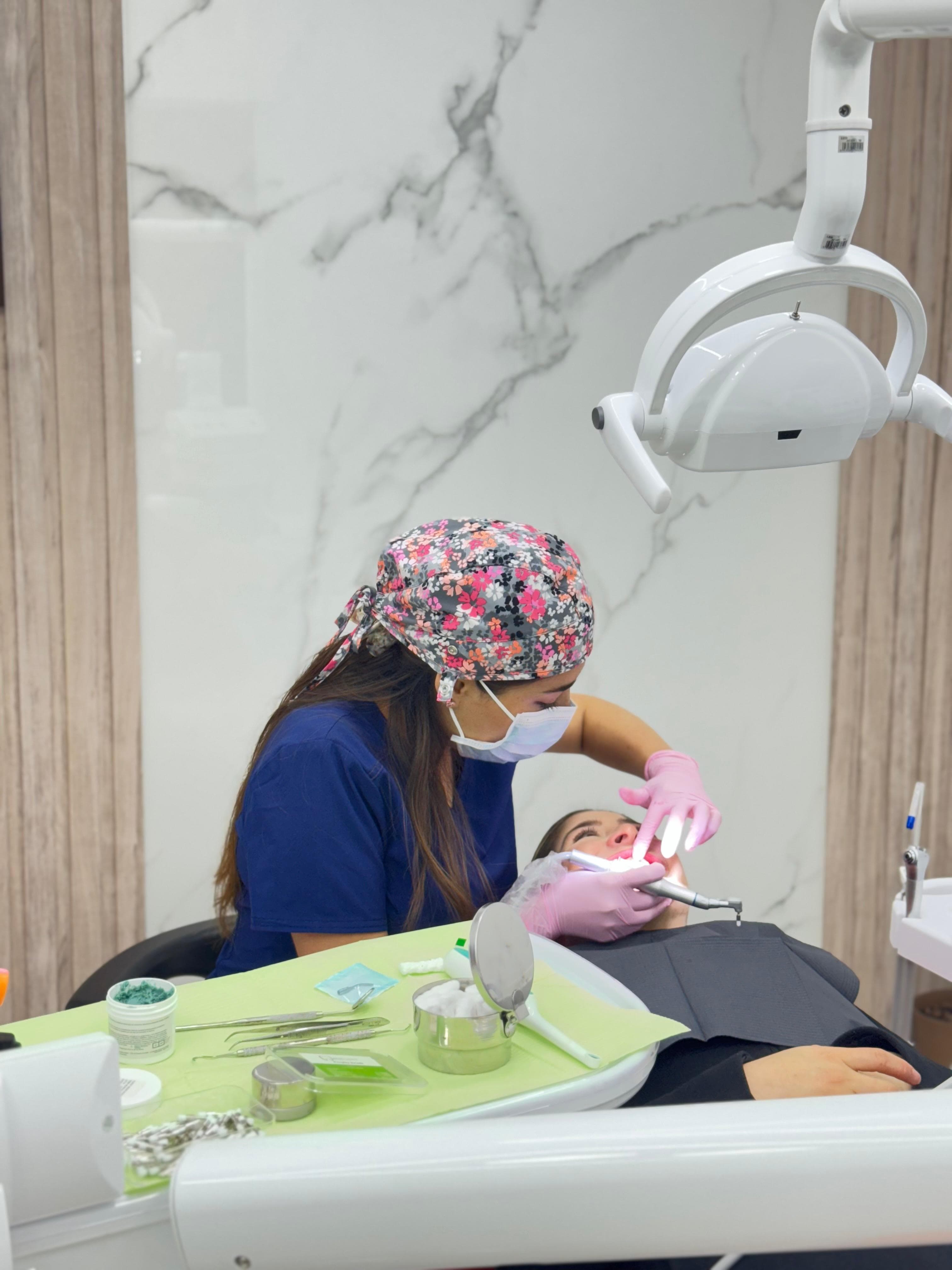 Dentist in a floral cap and pink gloves performs a procedure on a patient.