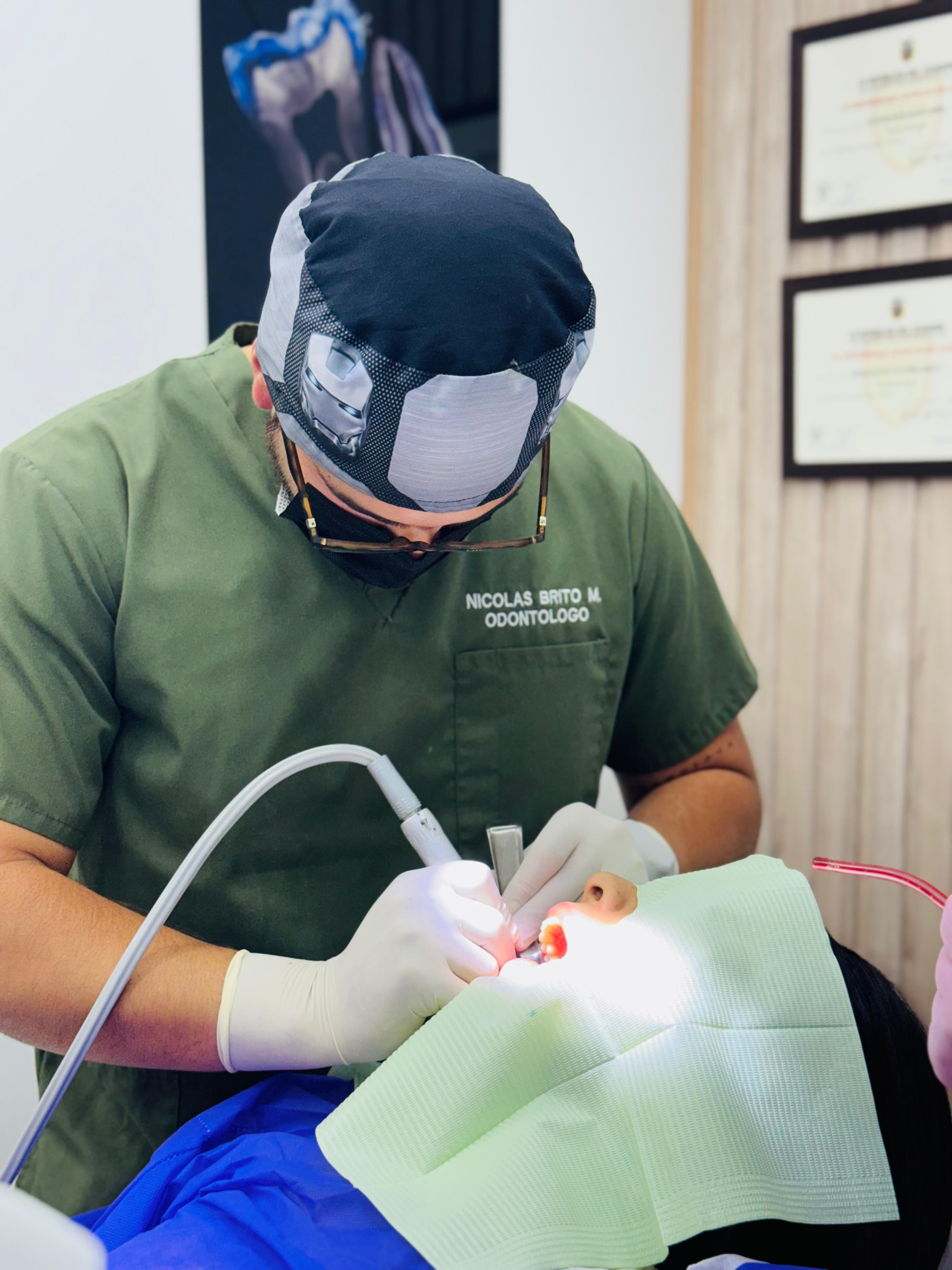 Dentist in green scrubs and surgical cap performs a dental procedure on a patient.