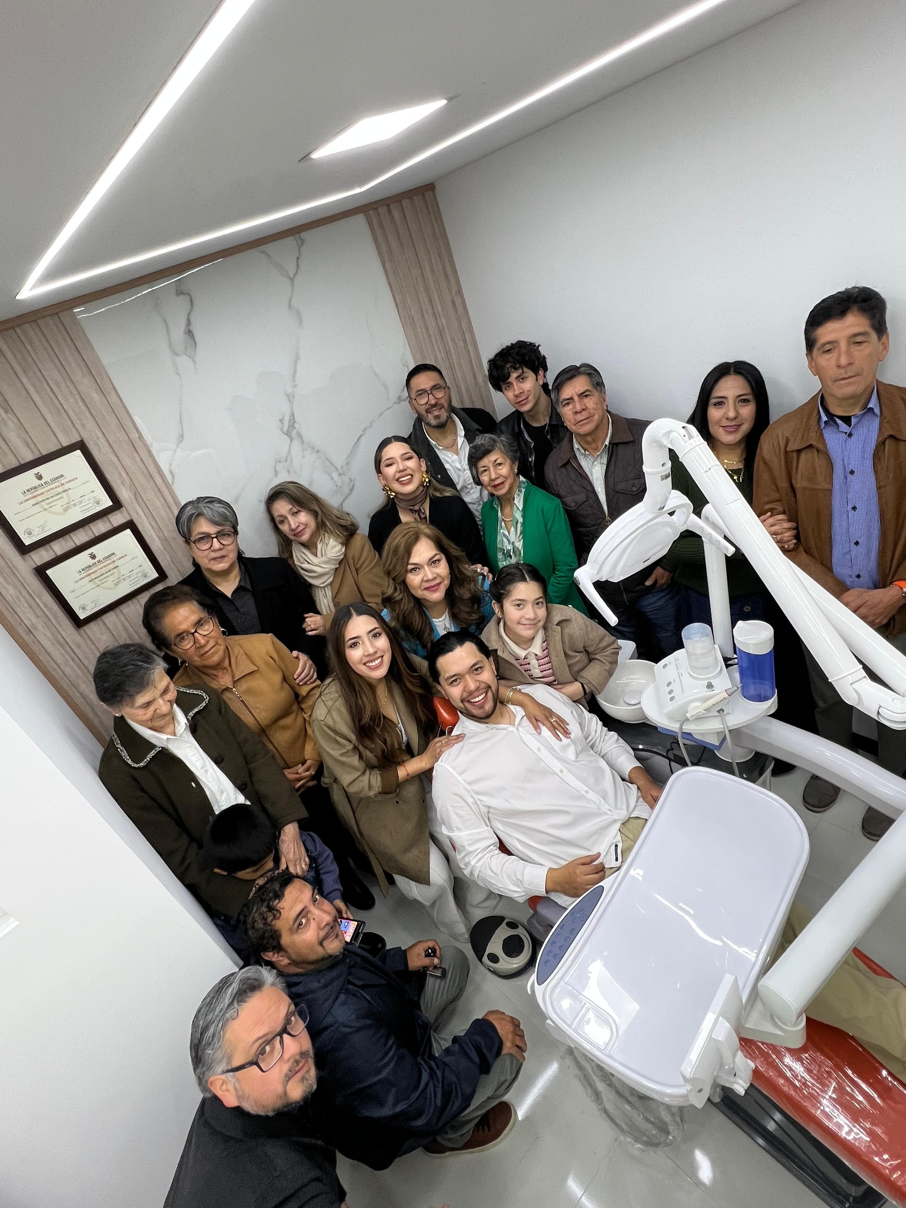 Large group of smiling people posing in a modern dental office around a seated man.