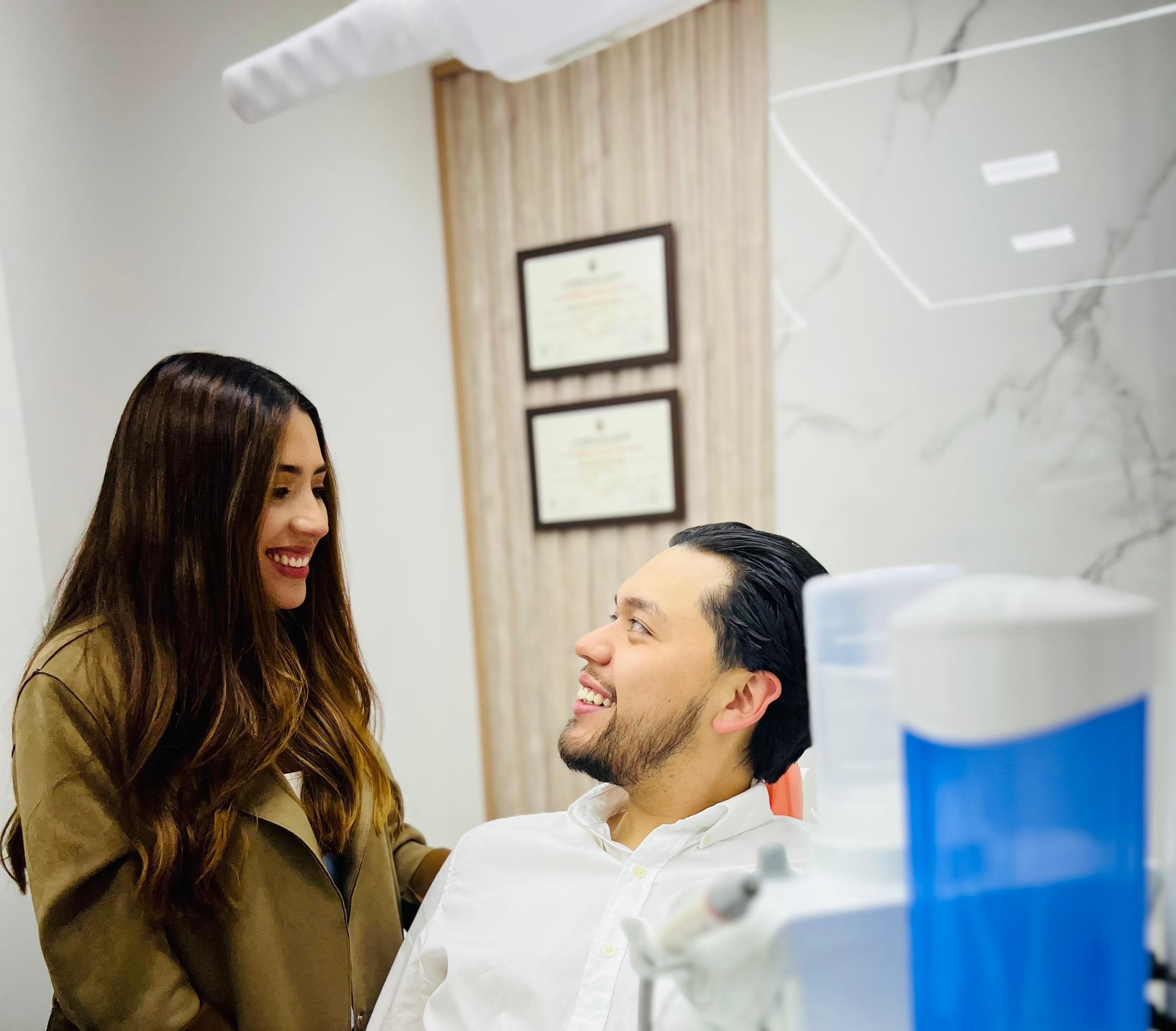 A smiling woman and man look at each other in a bright dental office.